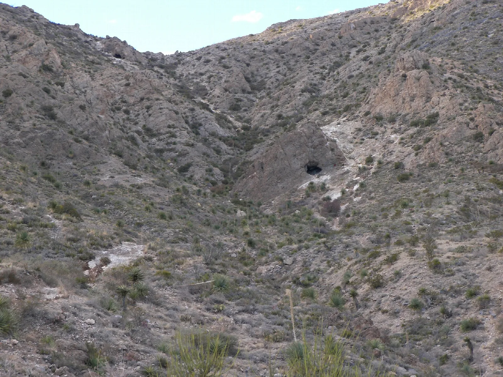 Rocky desert canyon with a dark cave opening on the slope