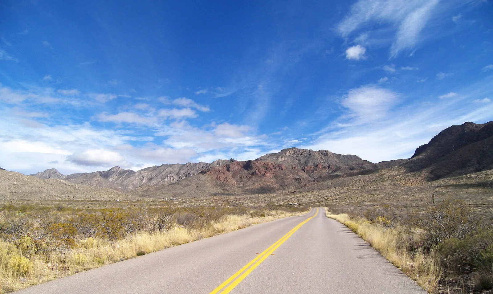 Paved road running toward rugged desert mountains under a blue sky