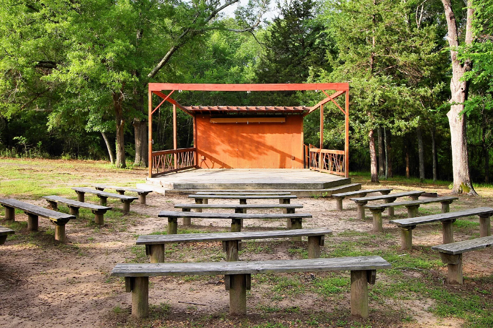 Outdoor amphitheater with a stage and wooden benches under trees