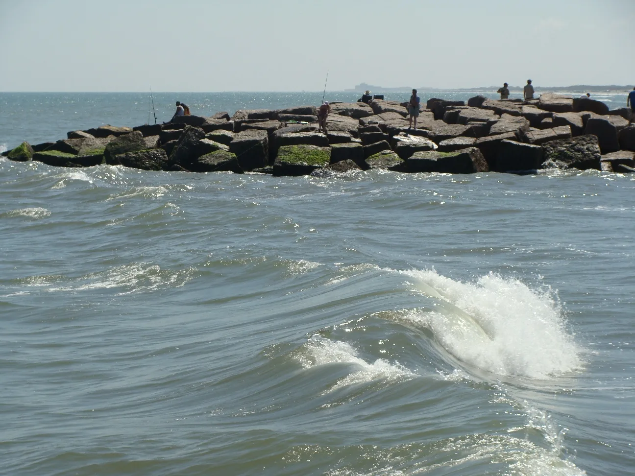 Waves breaking beside a rock jetty with people fishing
