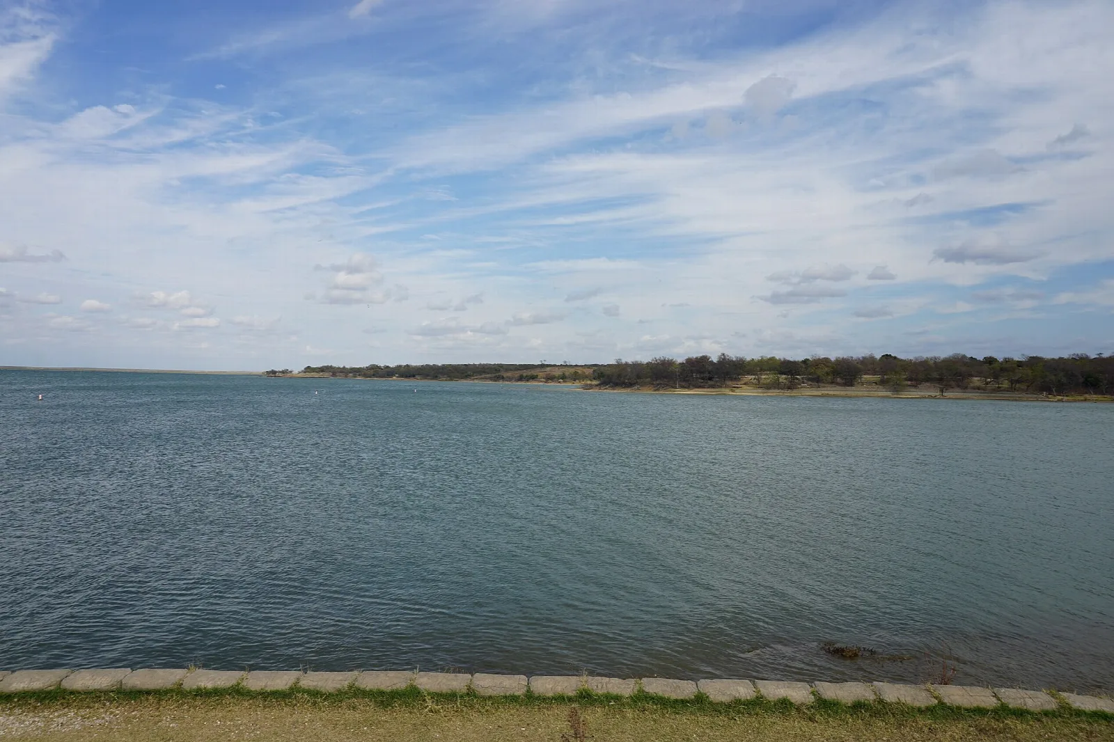 Wide lake with a distant tree-lined shore under blue sky