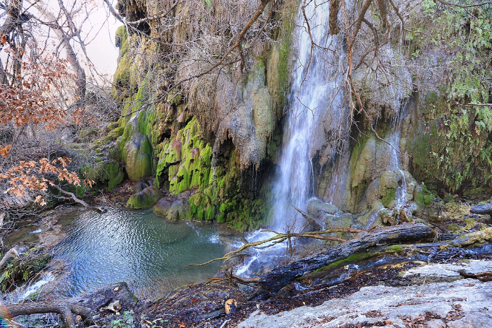 Waterfall dropping over mossy rock into a blue pool