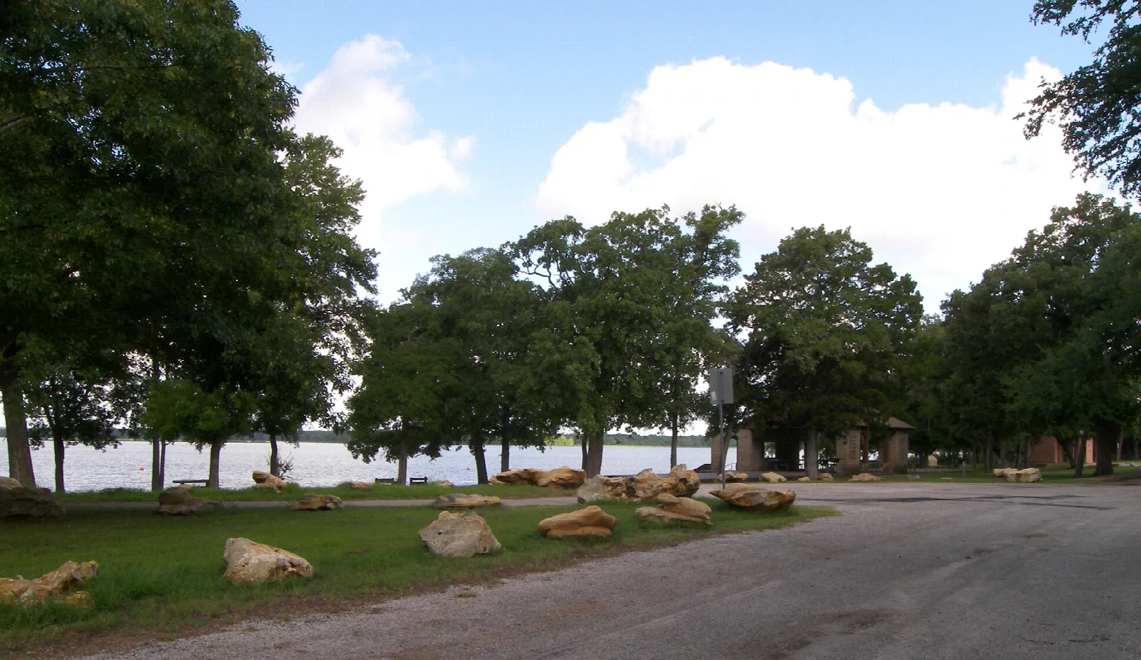 Park road beside a lake with scattered rocks and shade trees