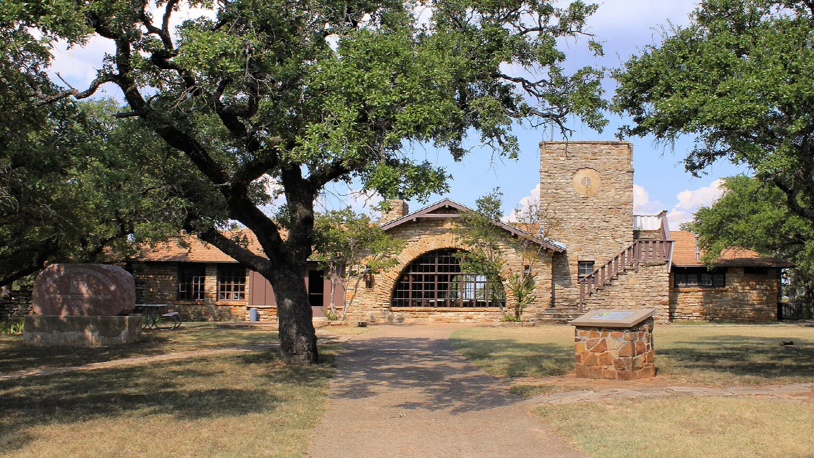 Stone clubhouse with arched windows under oak trees