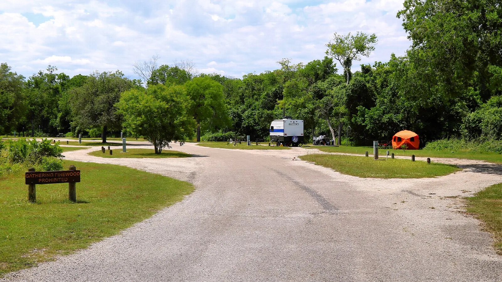 Paved camp loop road among green trees with an RV and tent