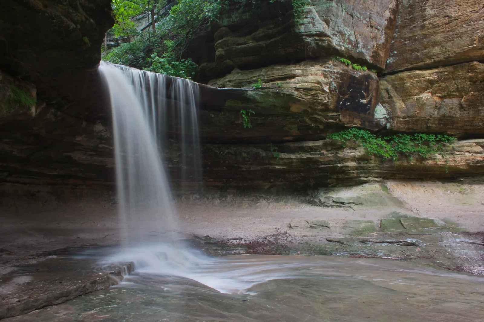 Waterfall dropping over a sandstone ledge into a shallow pool in a canyon