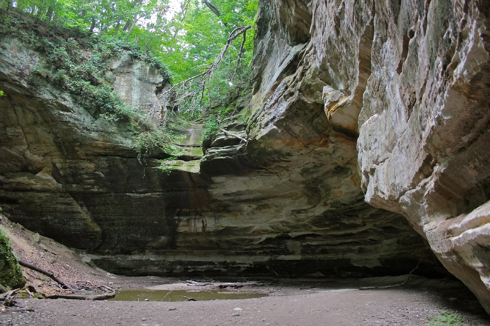 Wide sandstone overhang over a sandy canyon floor