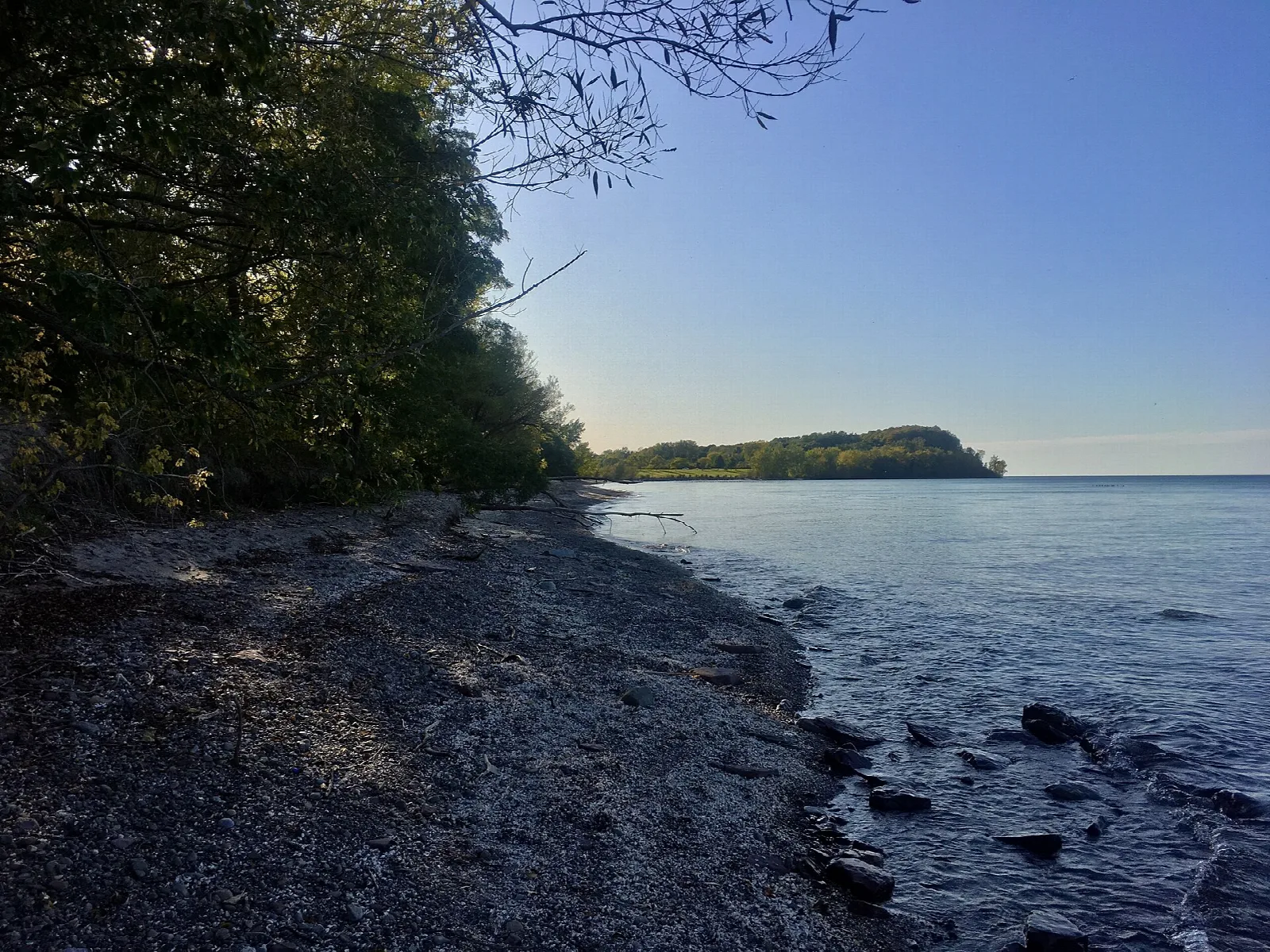 Dark rocky shoreline and still lake looking west toward a wooded point