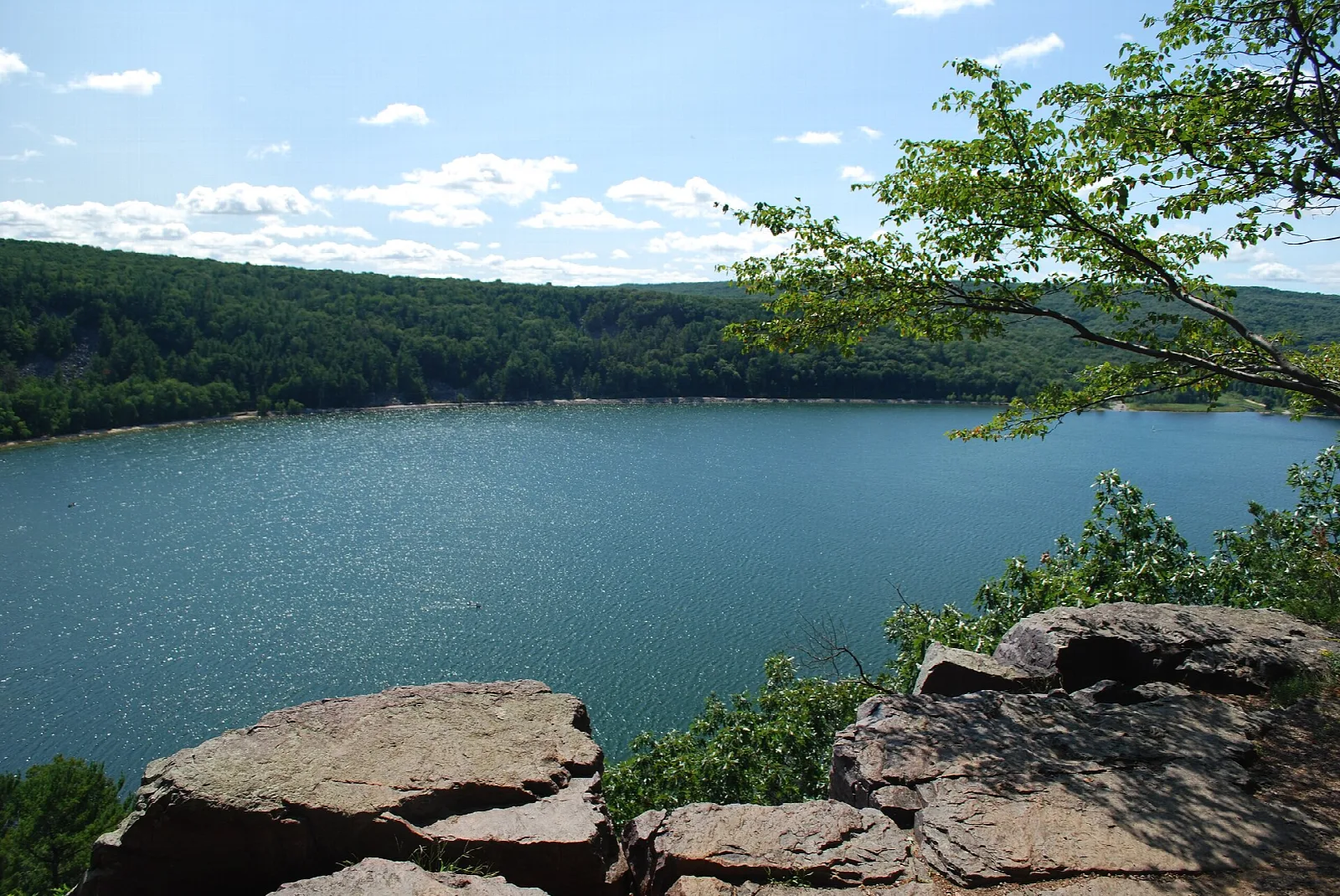 Lake seen from a rocky bluff edge with forested hills beyond
