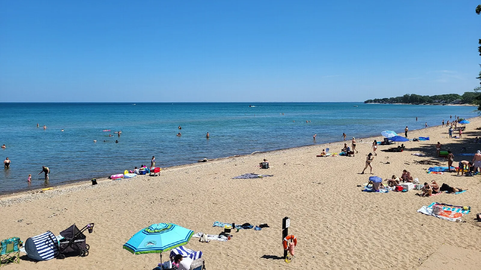 Sandy beach with swimmers and umbrellas along calm blue lake water