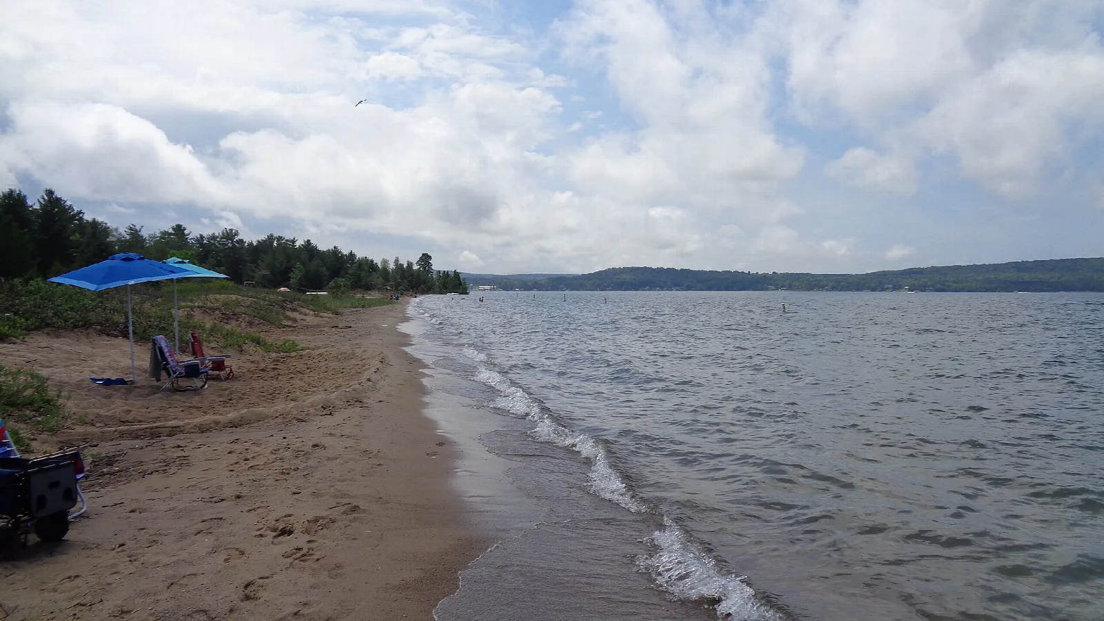 Wide sandy beach with chairs and an umbrella beside rippled lake water