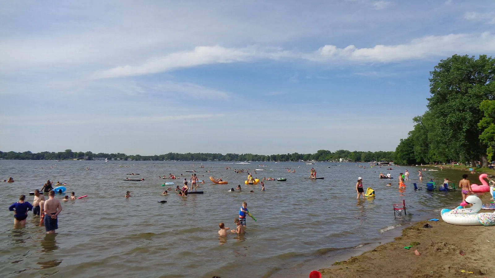 People wading and playing in shallow lake water at a sandy beach