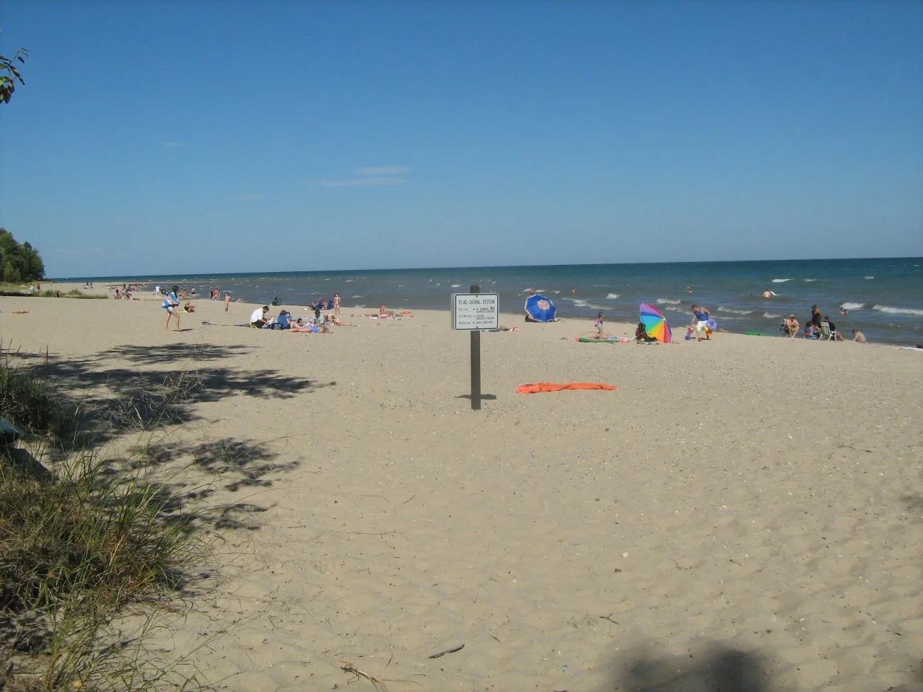Broad sandy beach with a small sign and people near the water