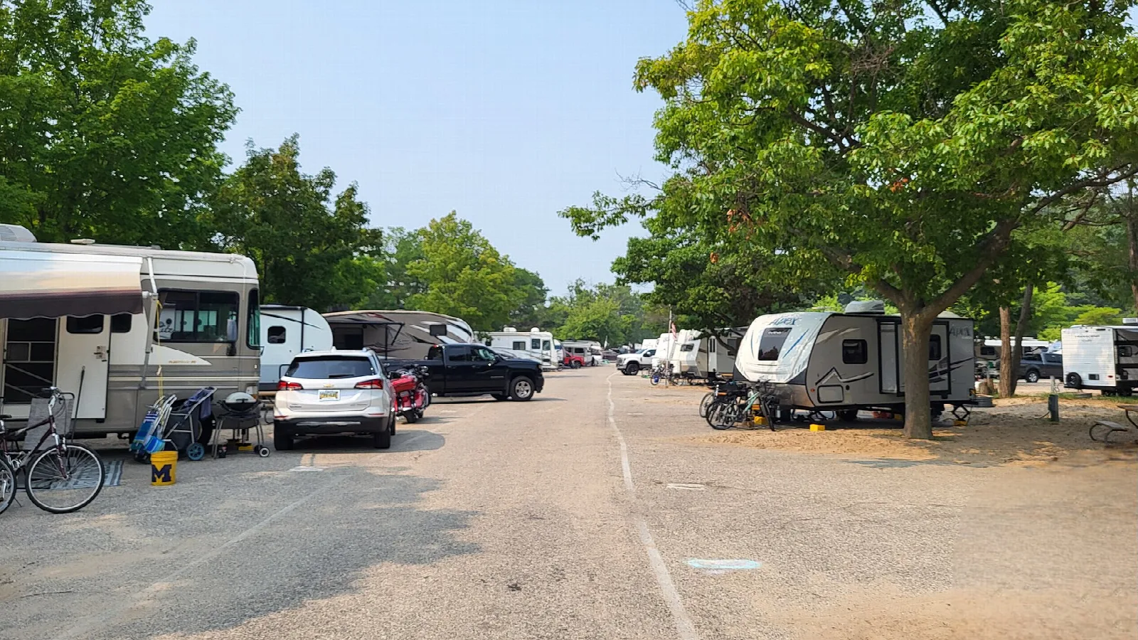 RVs and cars parked along a gravel lane under shade trees