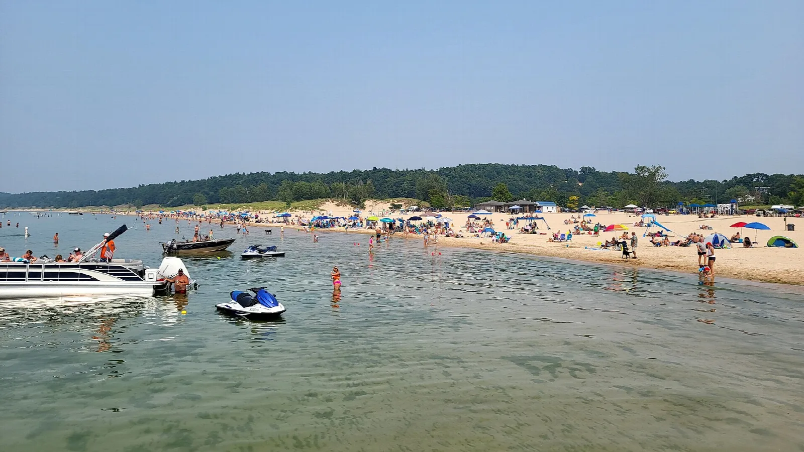 Crowded sandy beach with boats and jet skis in shallow green water