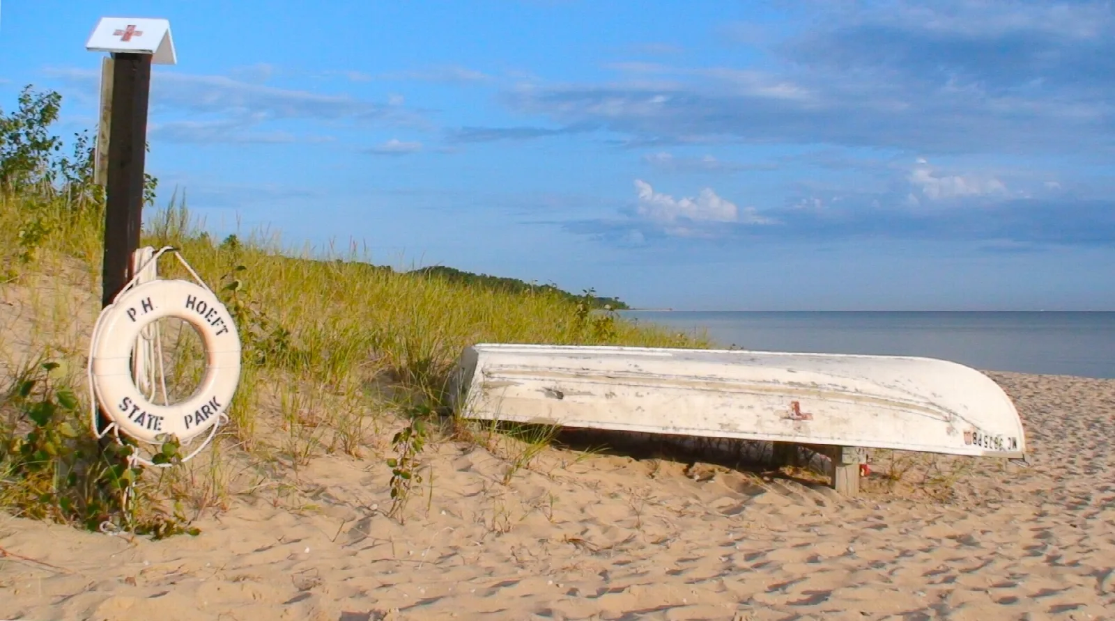 Upturned white boat and a life ring on a post on a dune beach