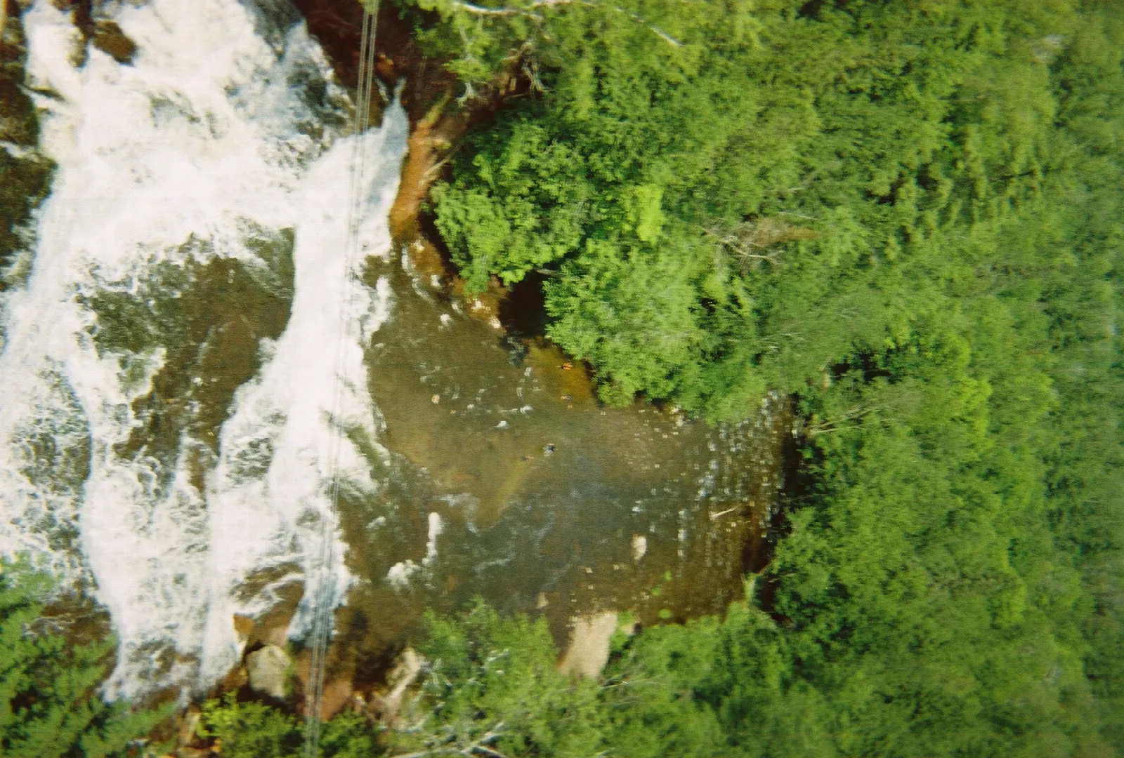 Looking down on white water running over rock beside green forest