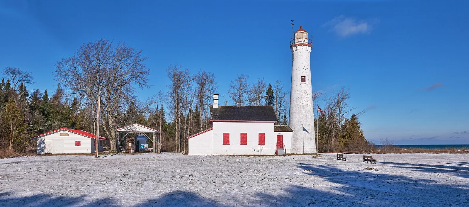 Lighthouse and white buildings across a snowy clearing with bare trees