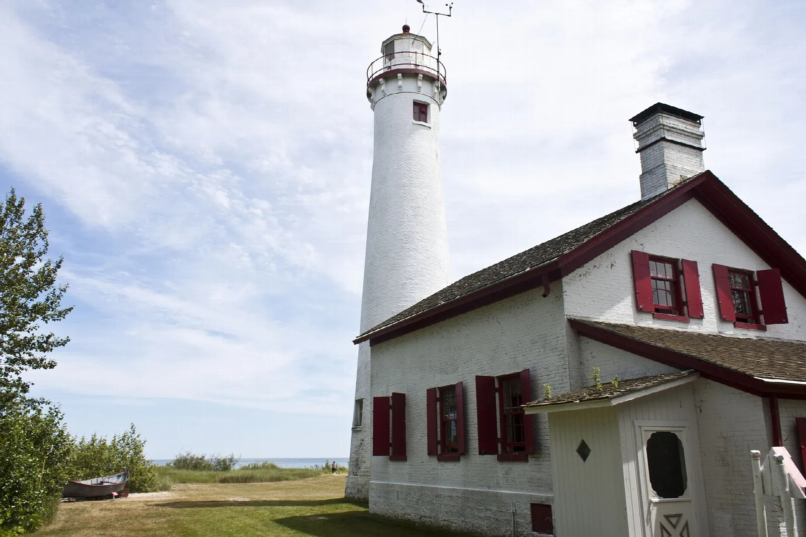 Tall white lighthouse tower and keeper's house with red shutters under blue sky