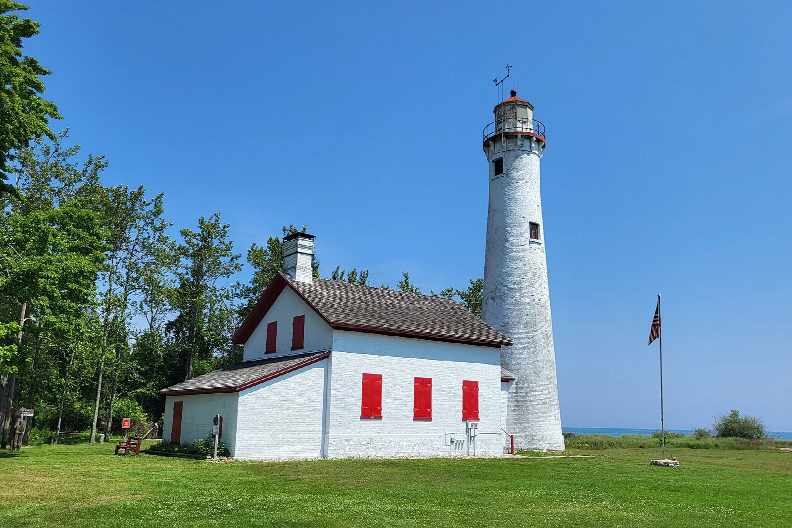 White lighthouse tower beside a keeper's house with red shutters on a green lawn