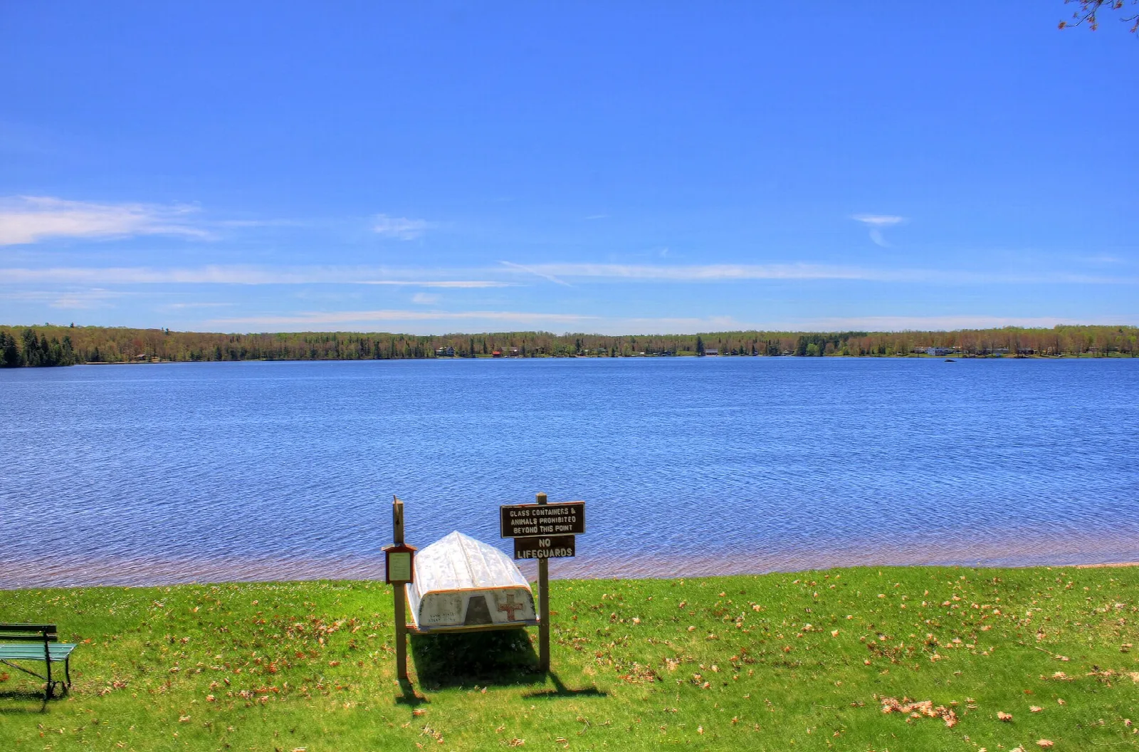 Upturned white boat on grass beside a wide blue lake
