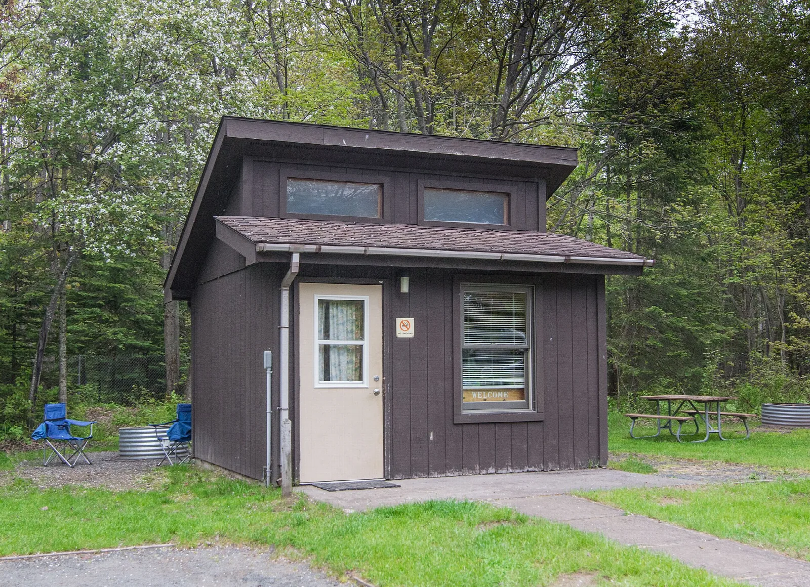Small brown cabin with camp chairs beside it in the woods