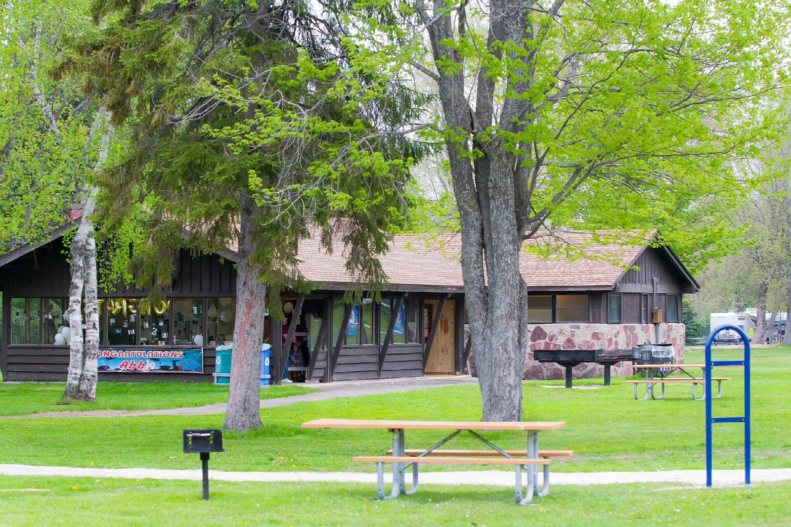 Log picnic shelter with a picnic table and grill on a green lawn