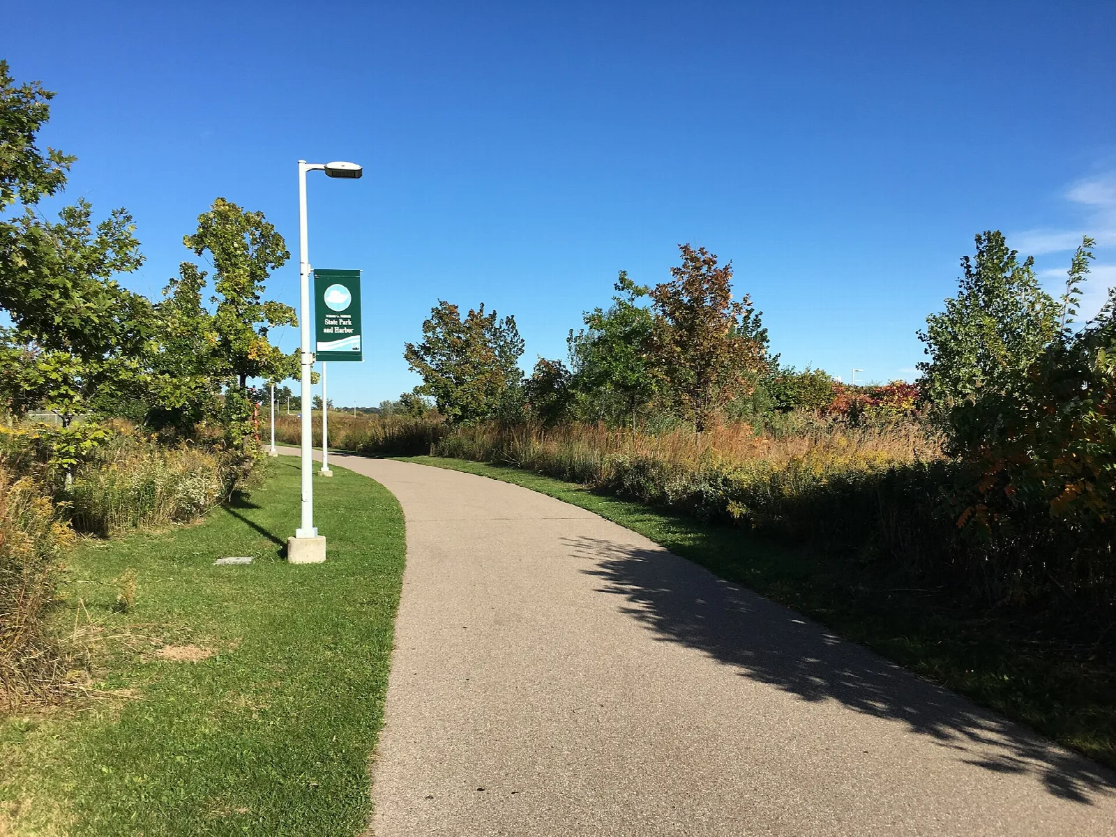 Paved riverwalk path lined with grass, shrubs and a lamp post