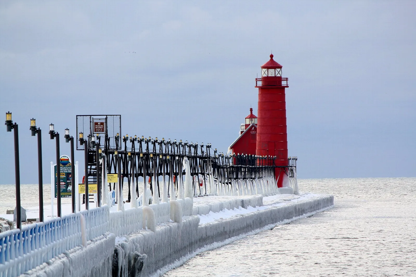 Ice-coated pier railing leading to a red lighthouse in winter