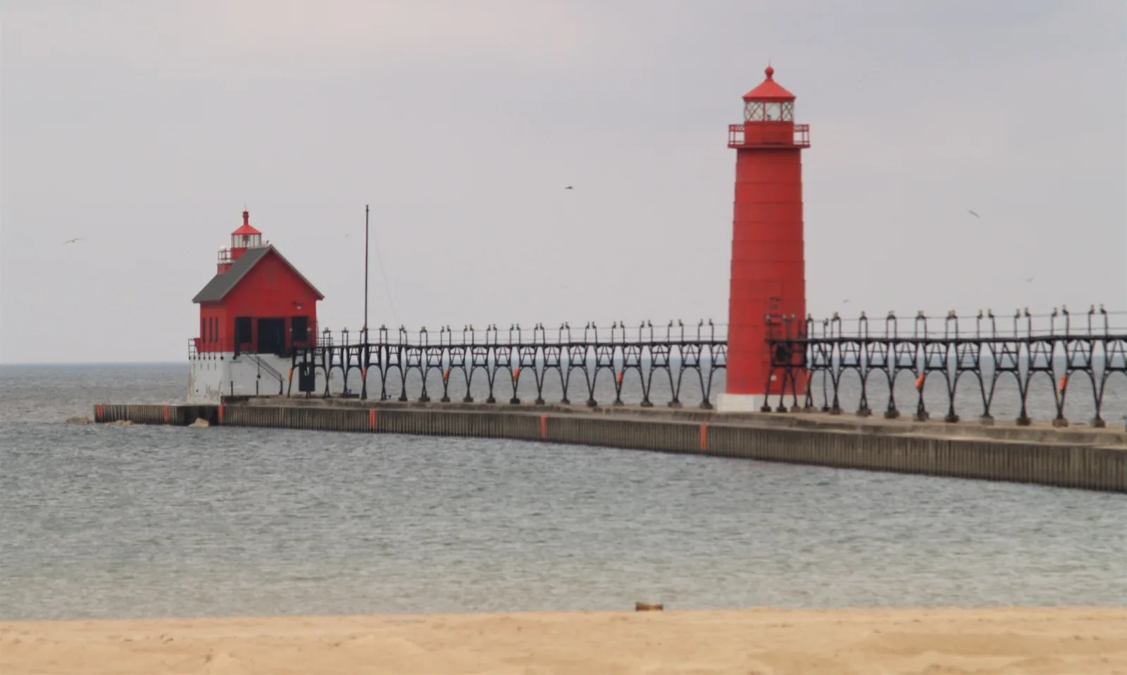 Red lighthouse and red-roofed light station on a long pier beside a sandy beach