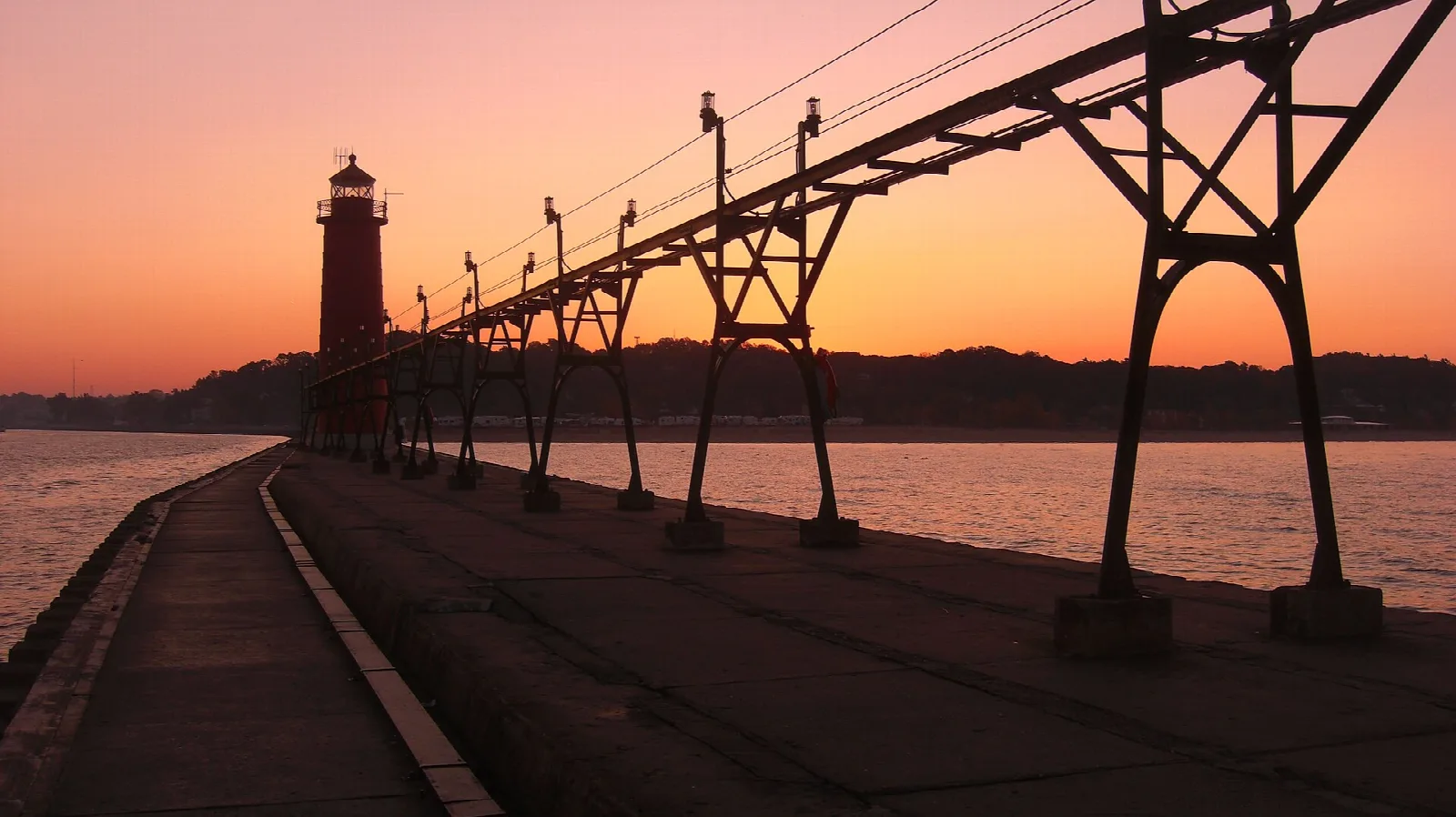 Pier walkway and lighthouse silhouetted against an orange sunset