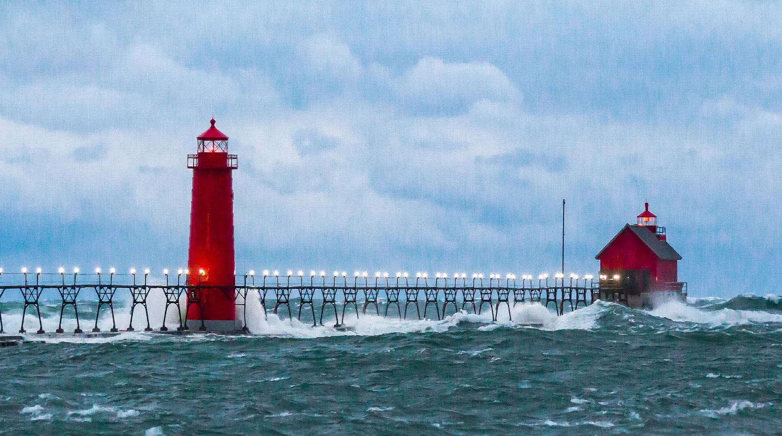 Red lighthouses on a pier with waves breaking and a stormy sky