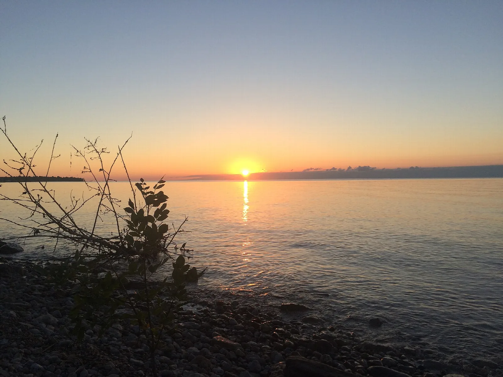 Sun setting over calm lake water seen from a rocky shore