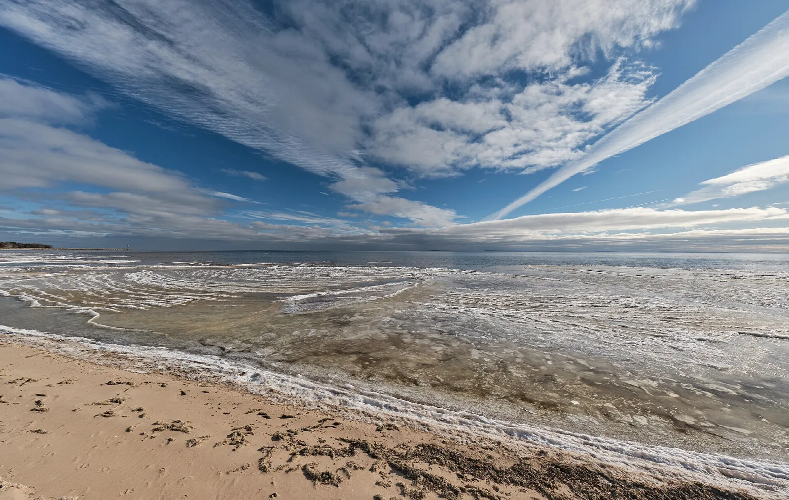 Flat icy shoreline with sand and a cloud-streaked sky over Lake Michigan