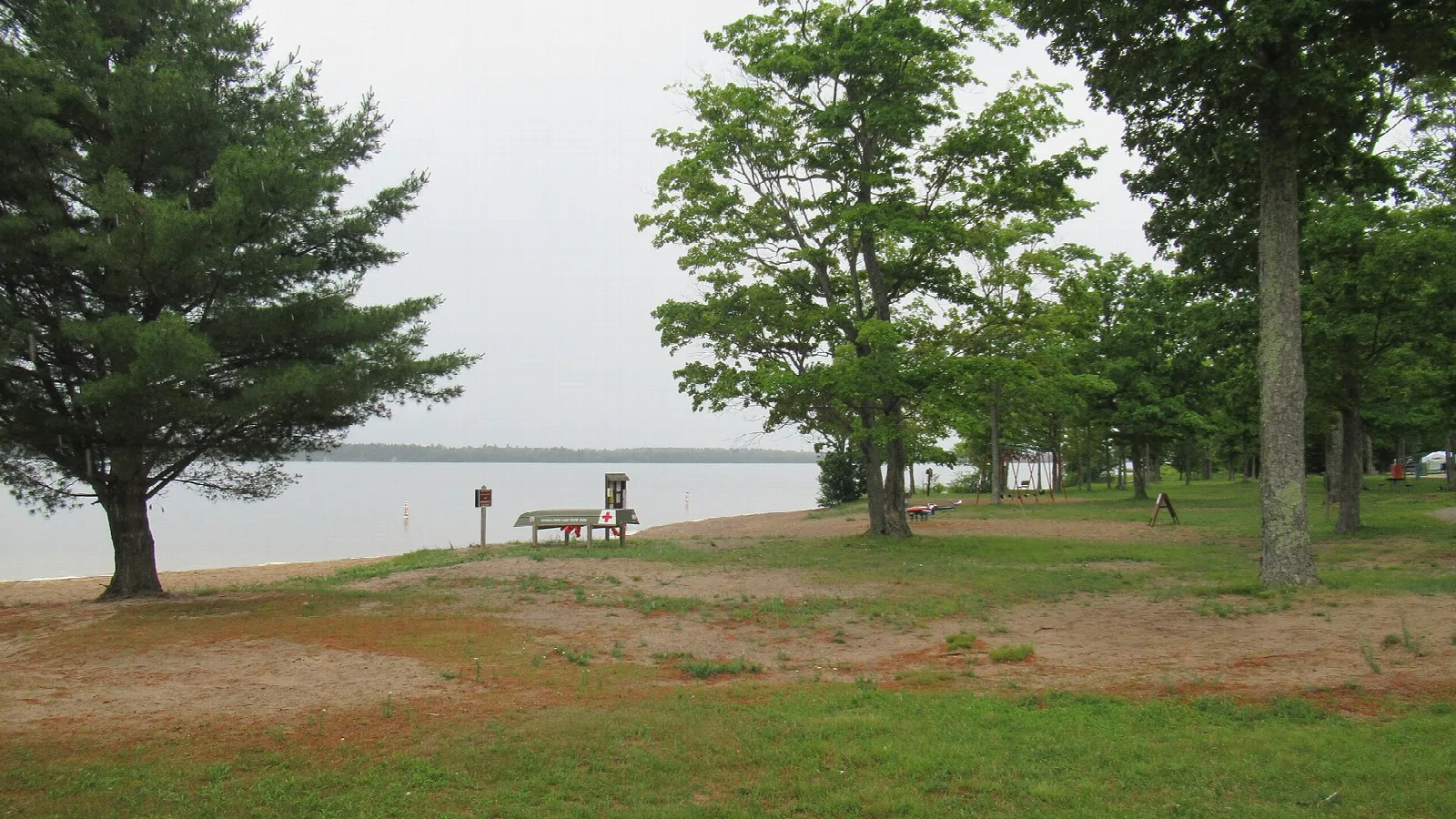 Grassy shore with picnic benches and trees beside a calm lake