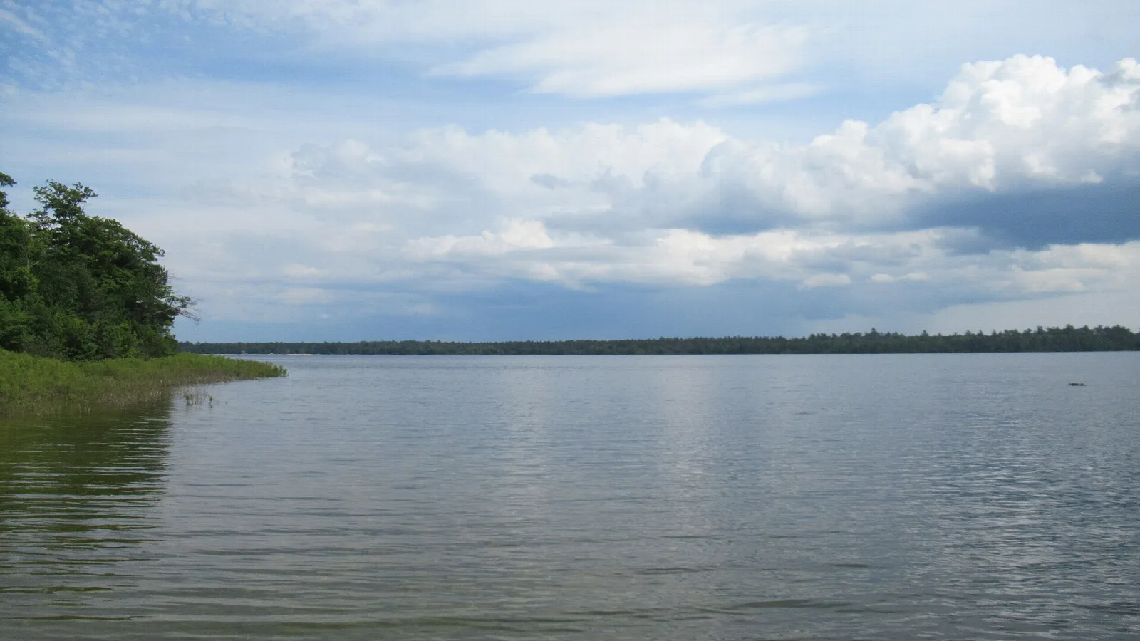 Calm lake with a wooded point and clouds over the water