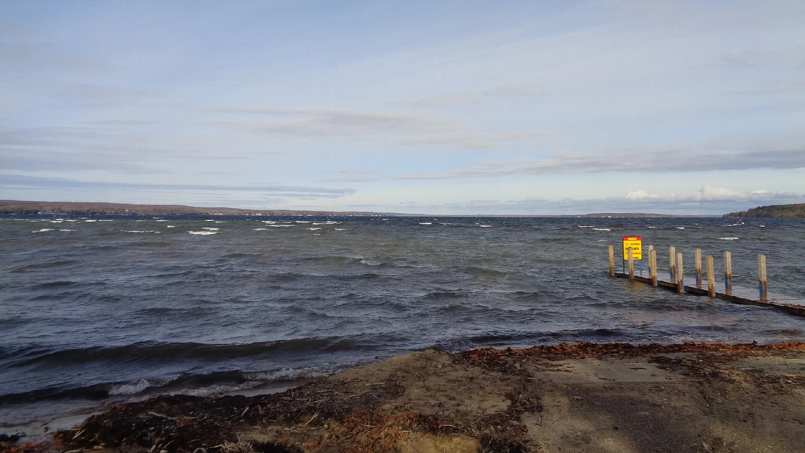 Choppy lake water with a small dock and rocky shore under a pale sky
