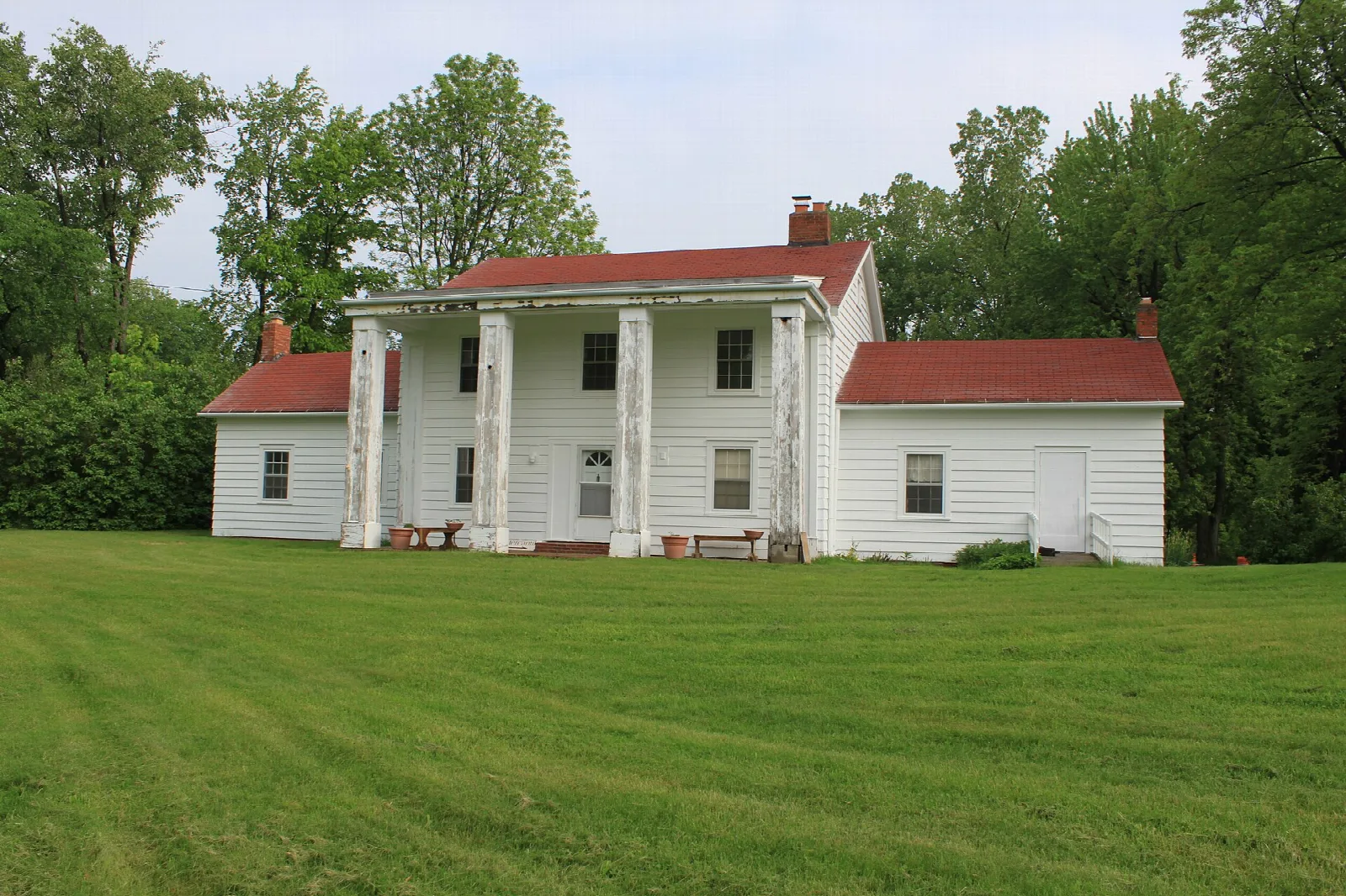 White house with columned porch and red roof across a green lawn