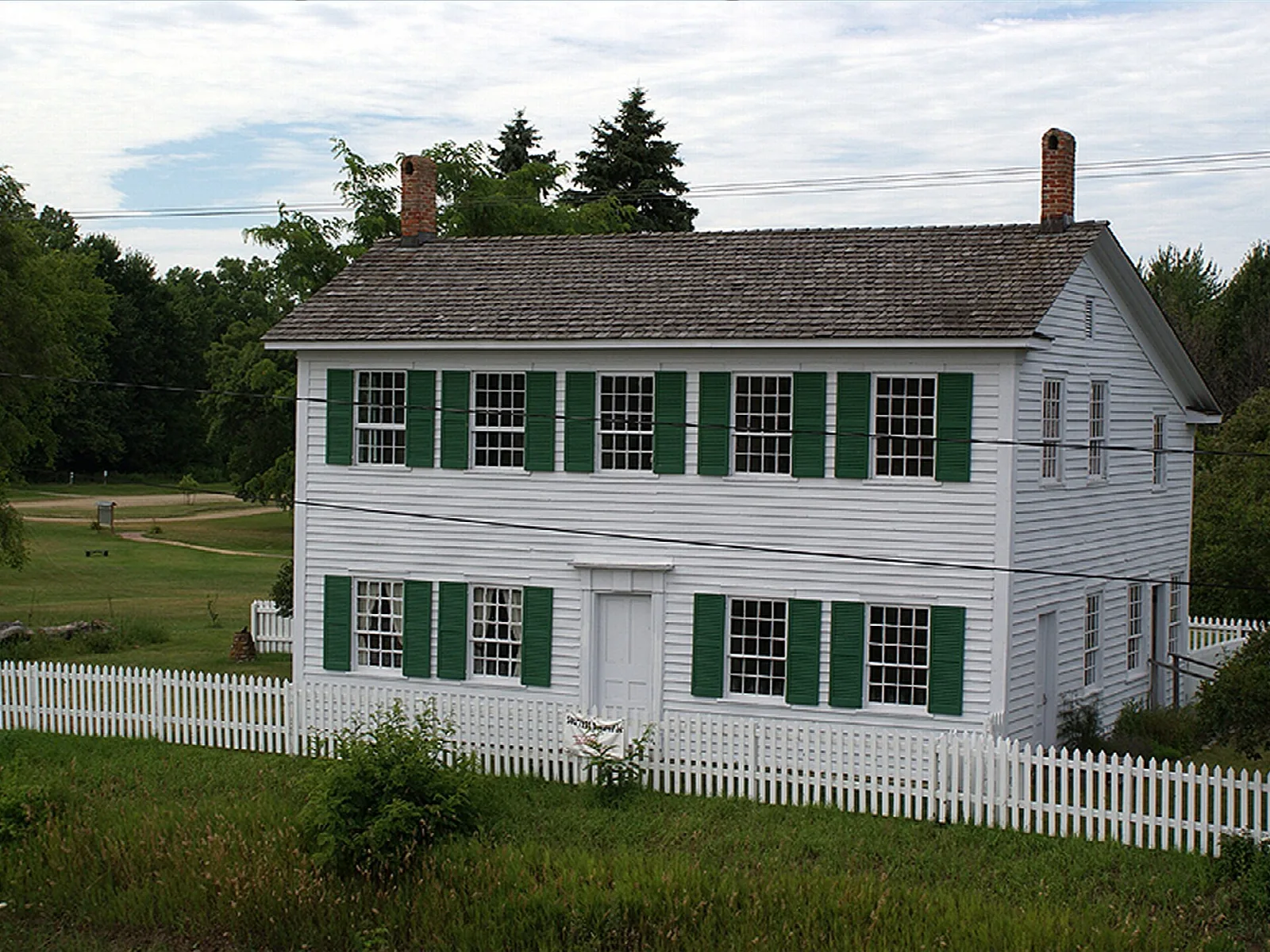 White two-story building with green shutters beside a picket fence