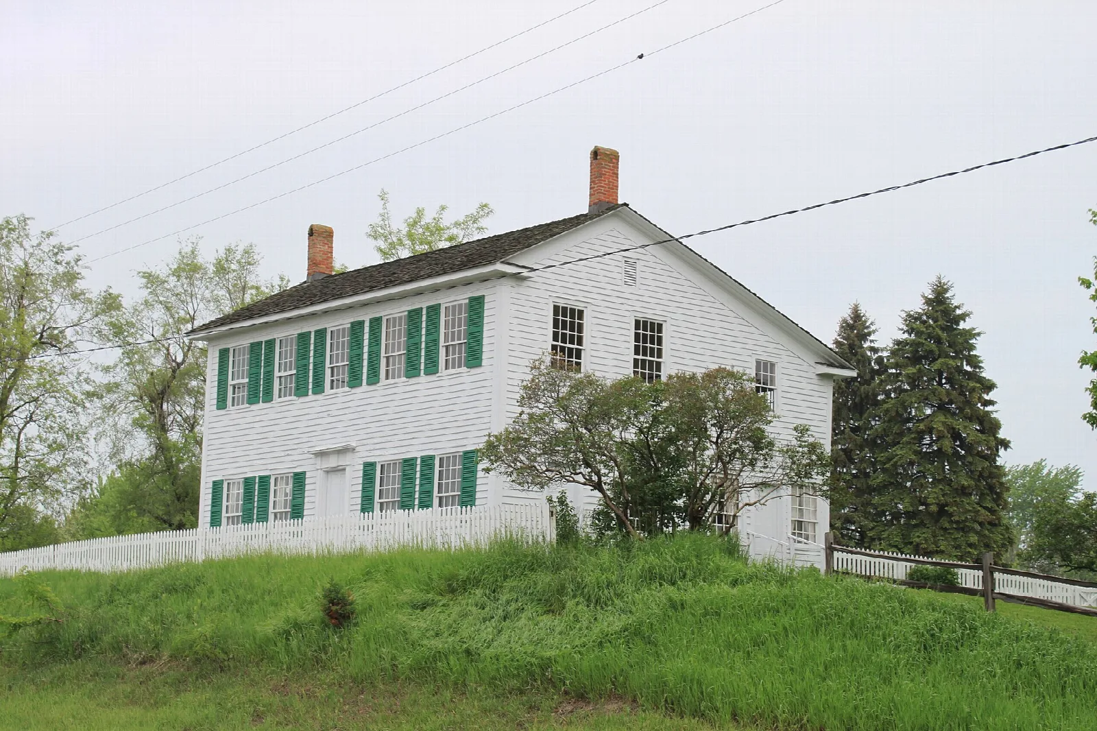 White farmhouse with green shutters on a grassy rise