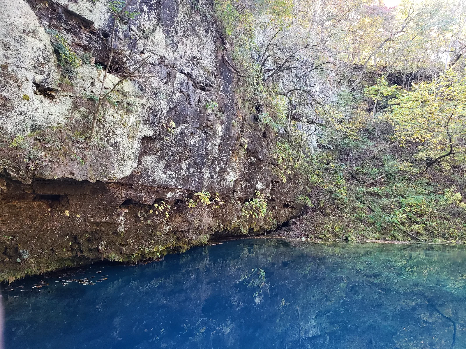 a deep dark blue spring at the bottom of a cliff of gray rock