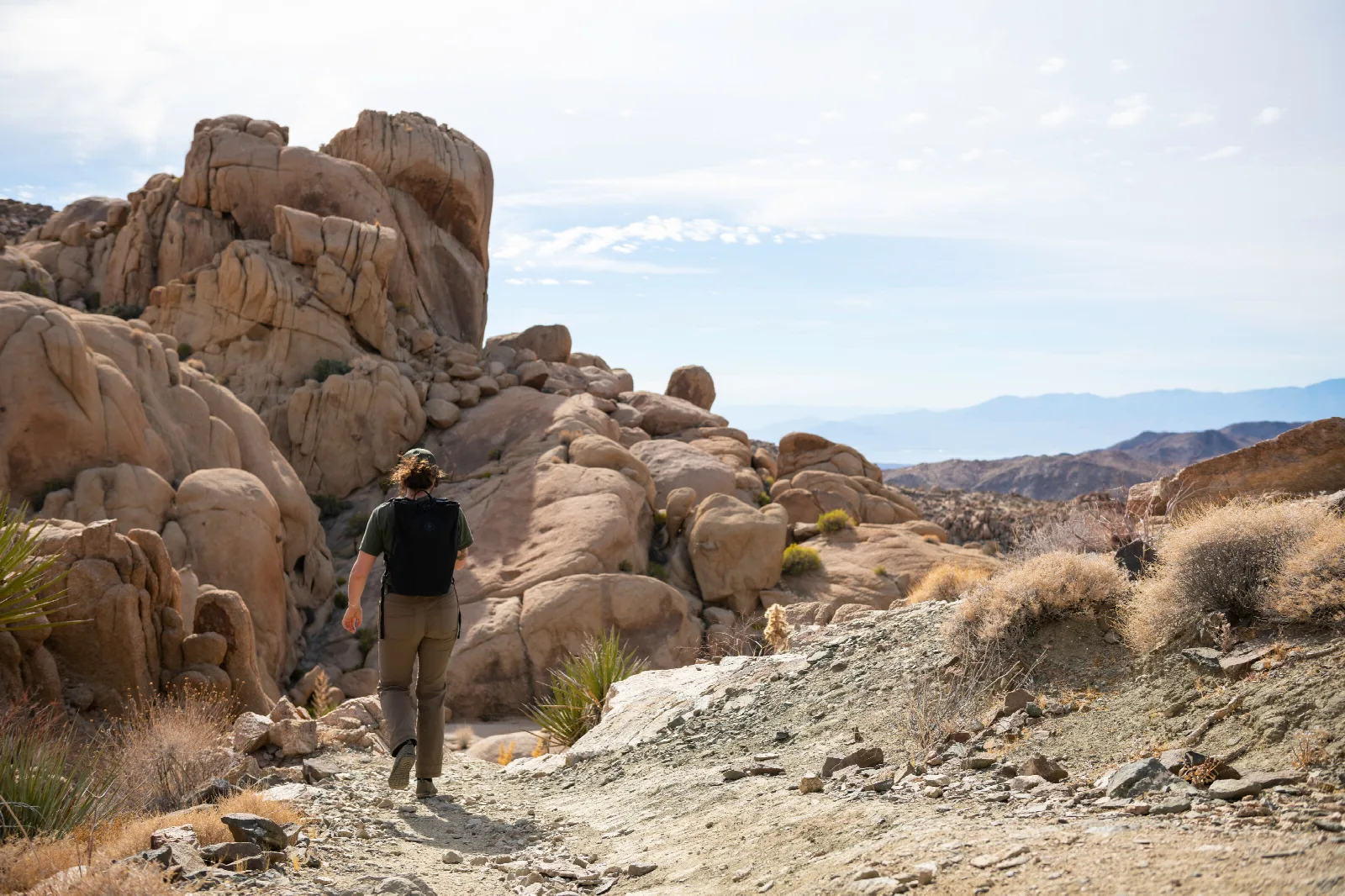 A hiker on a dirt trail headed towards a large rock formation in the distance.