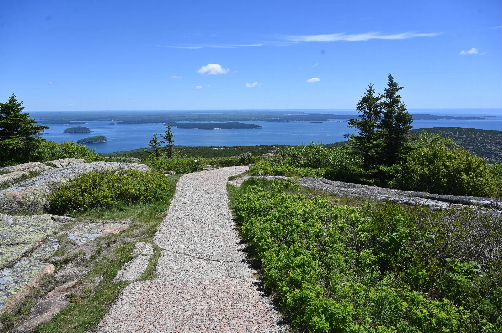 View of a paved trail on a mountain summit with islands and mountains extending to the far horizon.