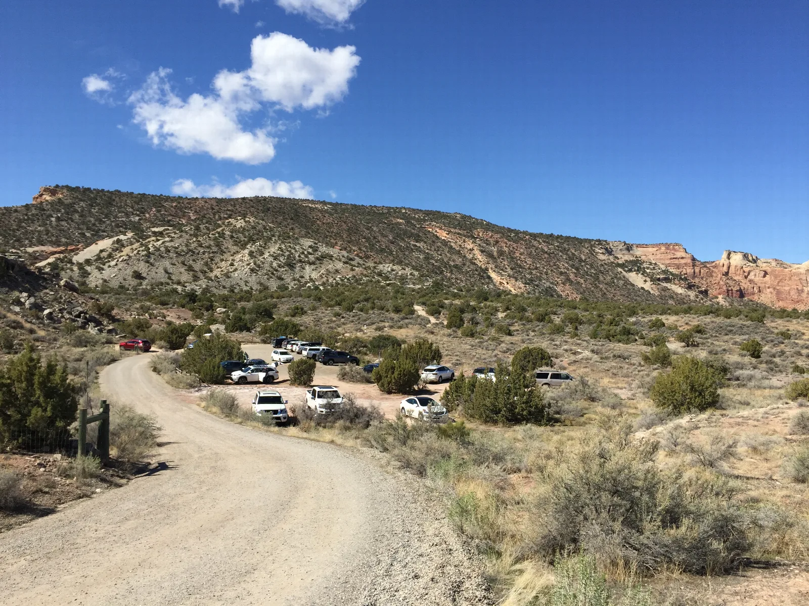 gravel road leads to dirt parking lot, backdrop of sparsely vegetated canyon slops