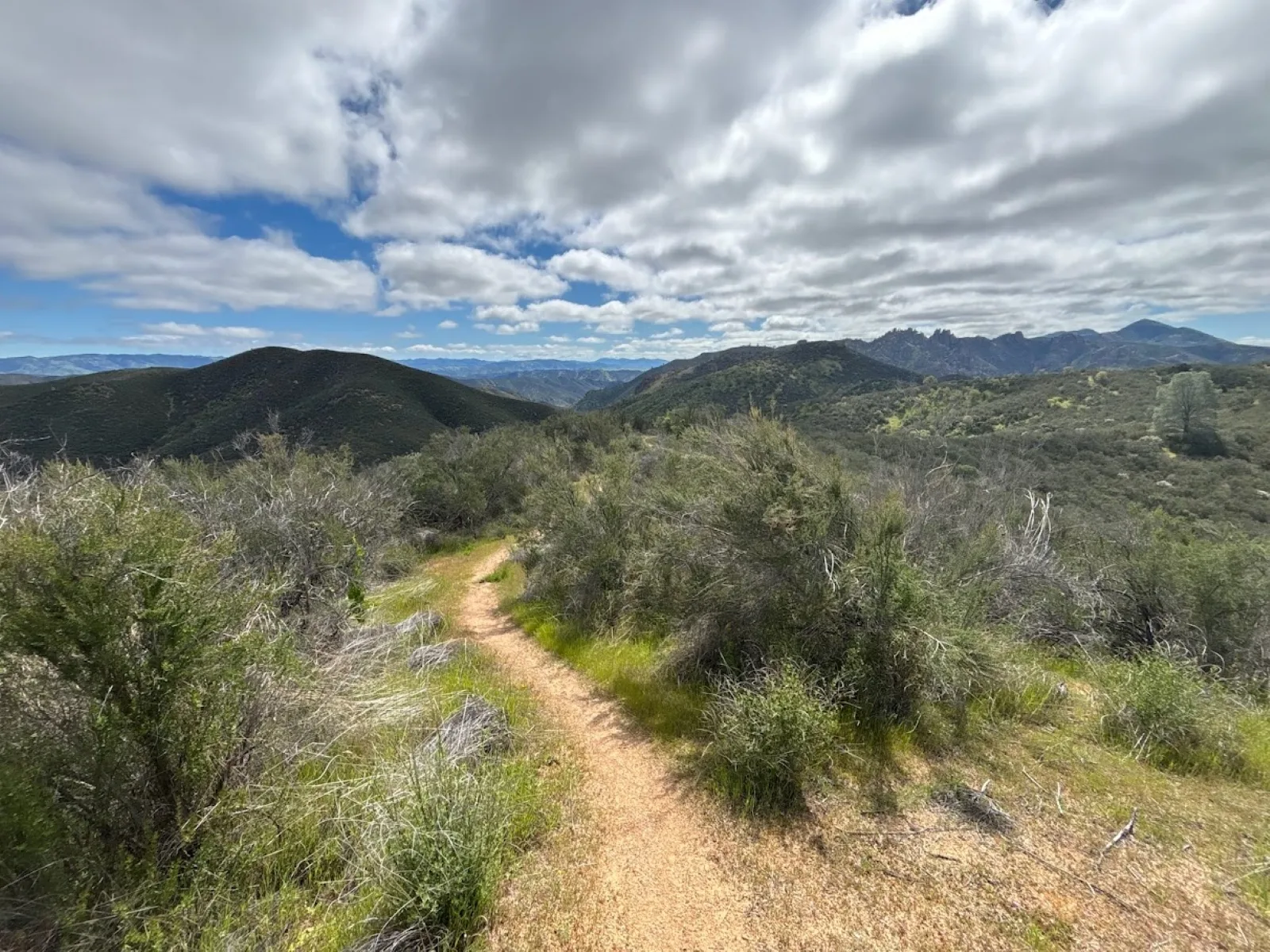 Trail leading through chaparral covered hills overlooking rock formations in the distance.
